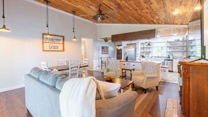 A spacious living area with a wooden ceiling, a dining table, and a kitchen in the background. - KING Bed+Cozy Farmhouse Cottage+Close to Trails (Bella Vista)
