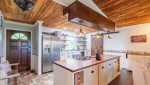 A kitchen with wooden ceiling beams, a central island with cabinets, a refrigerator, and pendant lighting. - KING Bed+Cozy Farmhouse Cottage+Close to Trails (Bella Vista)