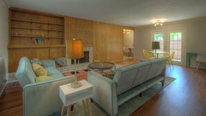 A living room with a sofa, a coffee table, and a fireplace. There is a dining area with a table and chairs. - Mid-Century Modern home in downtown Bartlesville (Bartlesville)