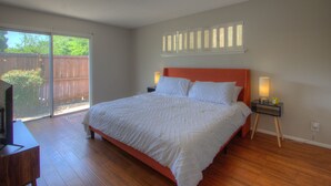 A bedroom with a large bed, a TV, and a sliding glass door leading to a backyard. - Mid-Century Modern home in downtown Bartlesville (Bartlesville)