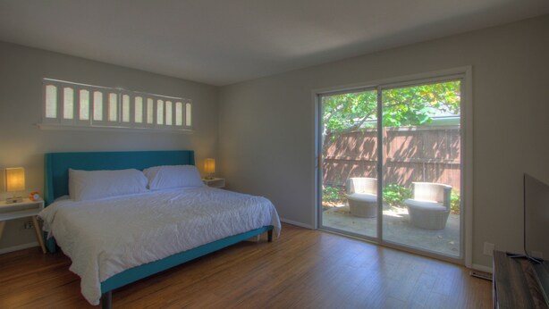 A bedroom with a bed, bedside lamps, a sliding glass door to a patio, and a view of the outdoors. - Mid-Century Modern home in downtown Bartlesville (Bartlesville)