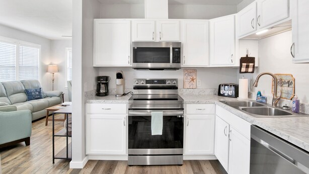 A modern kitchen with white cabinets, a stainless steel oven, a microwave, and a sink. - St-Navy Point Cottage (Pensacola)