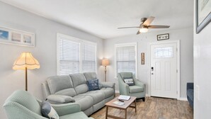 A living room with a sofa, two armchairs, a coffee table, a floor lamp, and a ceiling fan. - St-Navy Point Cottage (Pensacola)