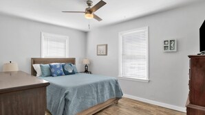 A bedroom with a bed, two bedside tables, a ceiling fan, and a dresser. - St-Navy Point Cottage (Pensacola)