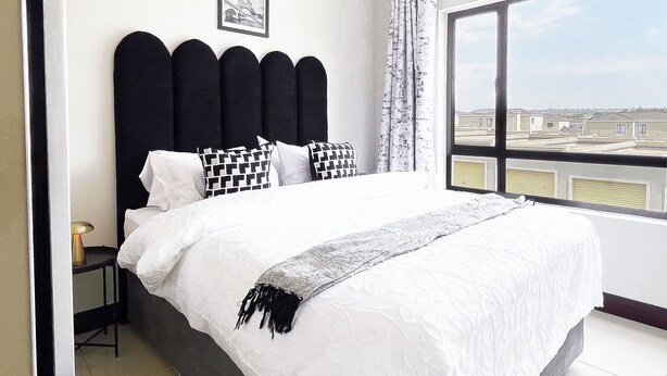 Un dormitorio con una cama grande, un cabecero negro y vistas a edificios a través de una ventana.