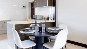 Un comedor moderno con una mesa redonda dispuesta para cuatro personas, rodeada de sillas blancas. Se observan un microondas y una cafetera en la encimera.