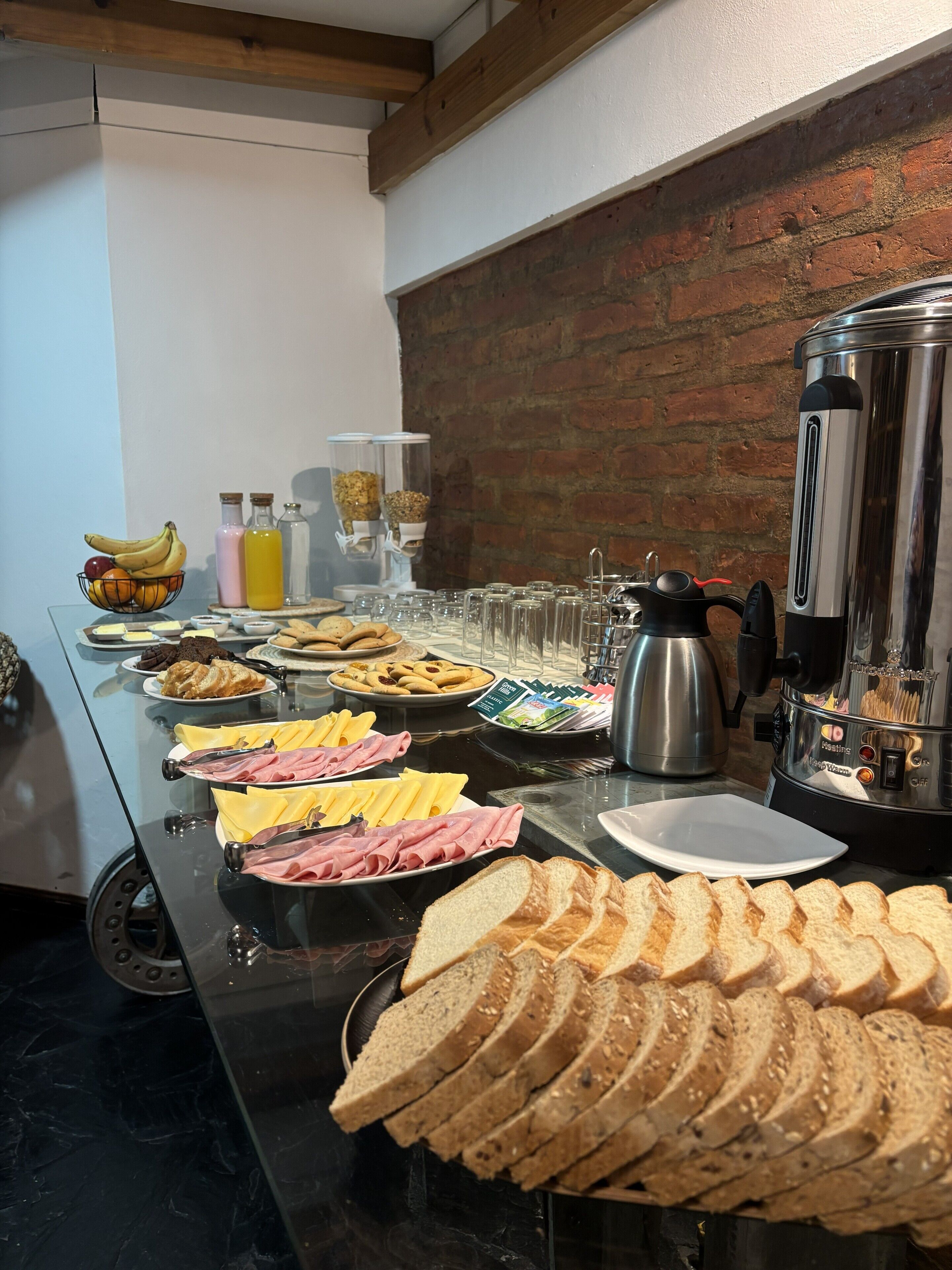 Un bufé con diversos alimentos, una cafetera y una pared de ladrillo al fondo.