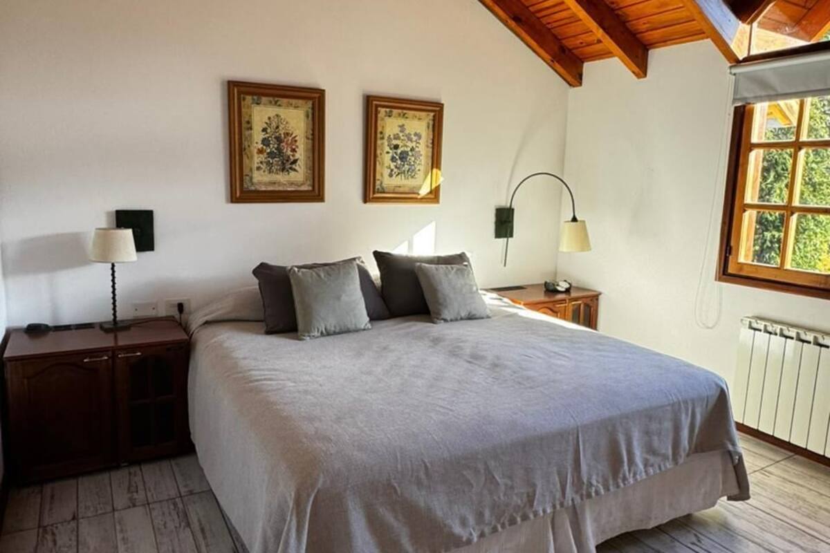 Un dormitorio con techo de madera, una cama grande, dos mesitas de noche y una ventana con vistas.