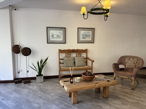 A living room with a wooden bench, a wicker chair, a table with a candle, and two framed pictures on the wall. - Hostería Plaza Mayor  (San Martín de los Andes)