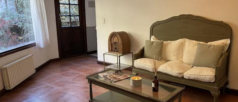 A living room with a green sofa, a glass coffee table, a wooden side table, and a radiator.