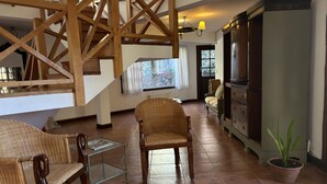 Un salón amplio con techo alto, escaleras de madera, muebles de mimbre, una mesa de centro de vidrio y una planta en maceta.