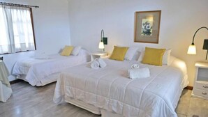 Habitación de hotel con dos camas, cada una con ropa de cama blanca y almohadas amarillas. Hay mesitas de noche con lámparas, un cuadro en la pared y una ventana con cortinas.