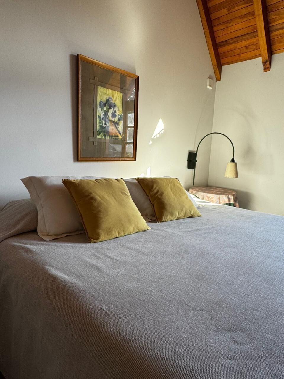 A bedroom with a bed, two pillows, a nightstand, a lamp, and a framed picture on the wall.