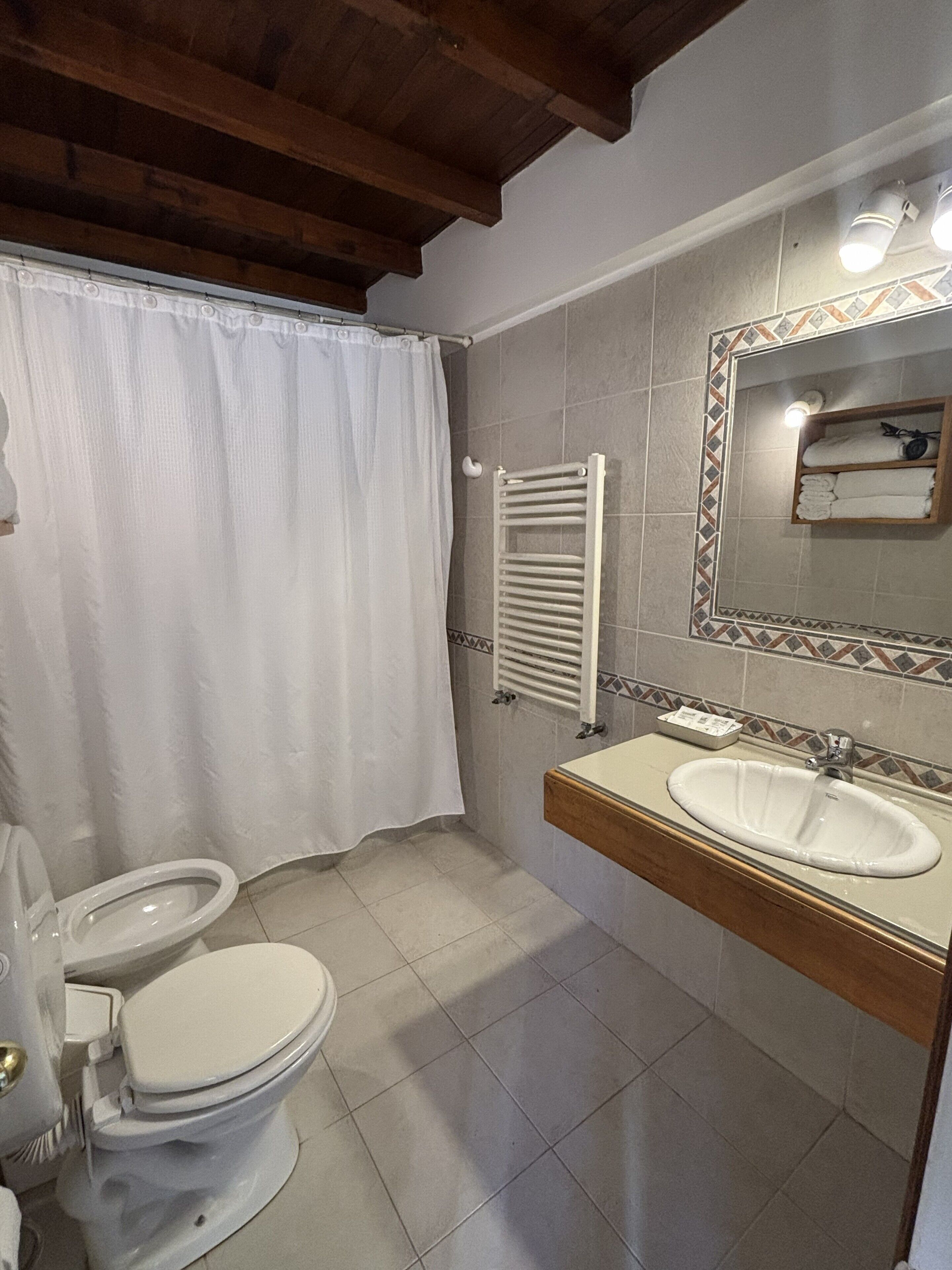 Ein Badezimmer mit Toilette, Waschbecken, Duschvorhang, Handtuchhalter und einem Spiegel mit Fliesenverkleidung.