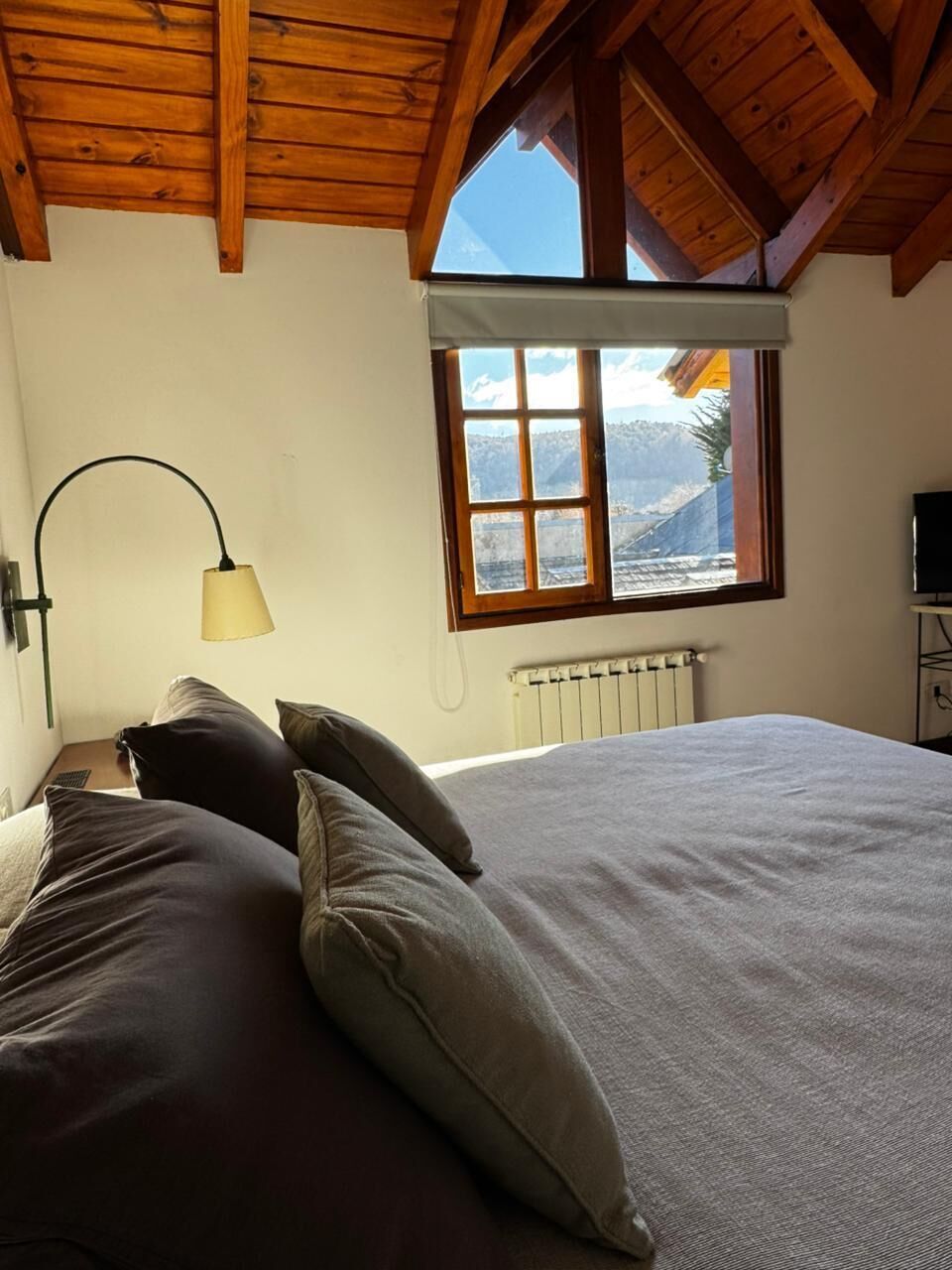 Une chambre à coucher avec un lit, des oreillers, une lampe, une fenêtre donnant sur un paysage agréable et un radiateur.