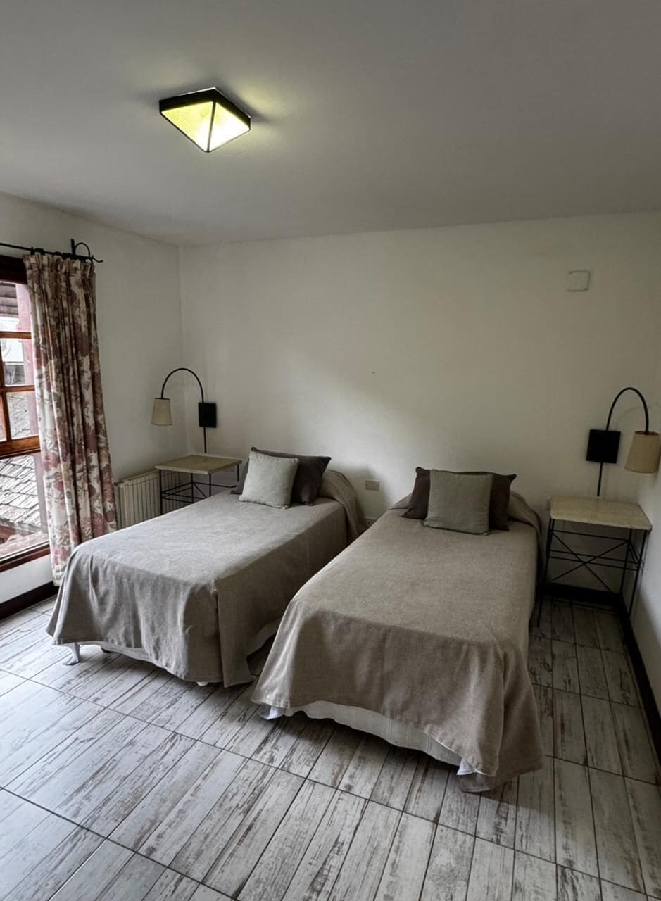 Une chambre avec deux lits, une petite table, une lampe et une fenêtre avec des rideaux.
