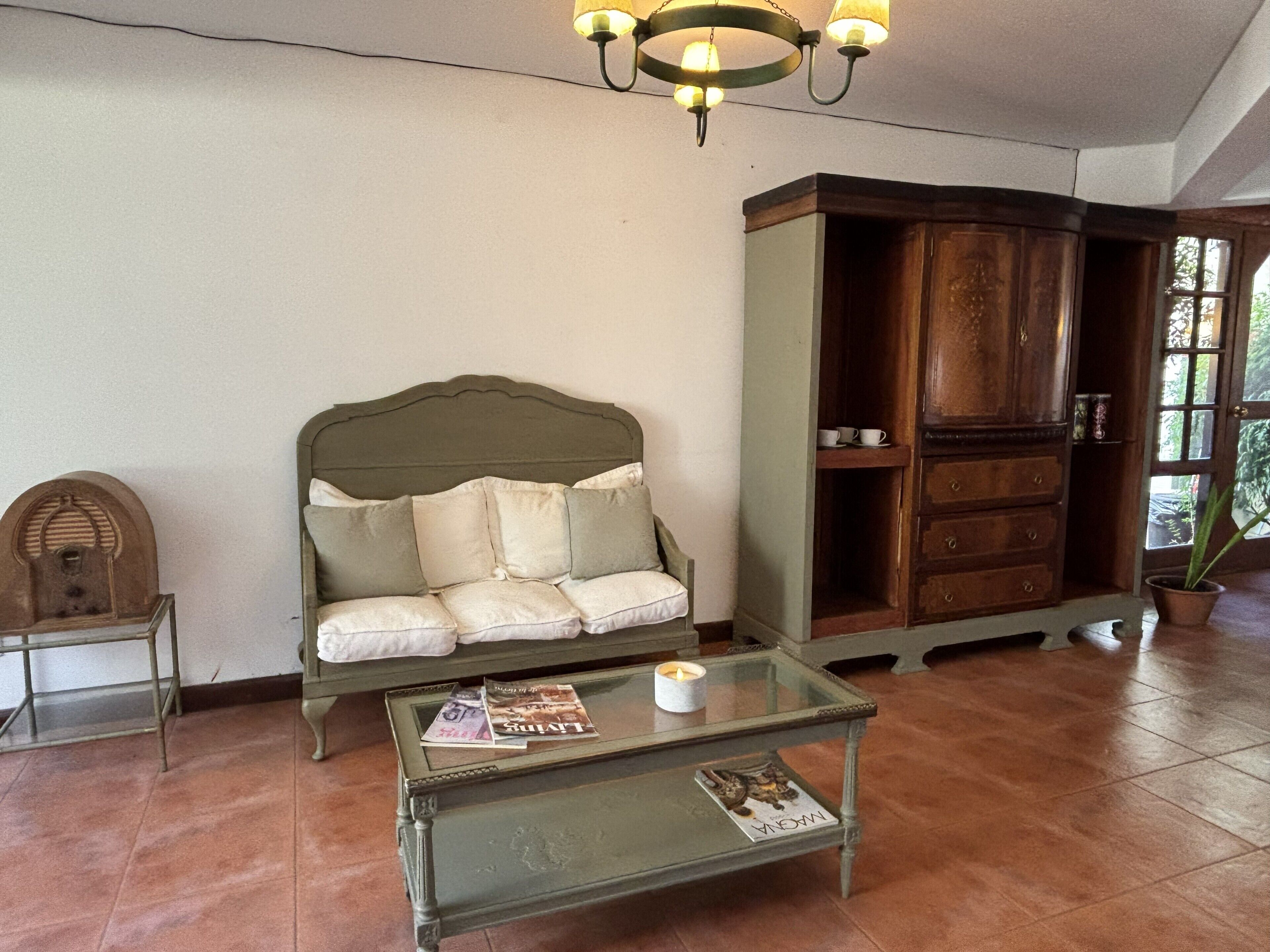 A room with a green sofa, a glass coffee table, a wooden cabinet, and a hanging light fixture.