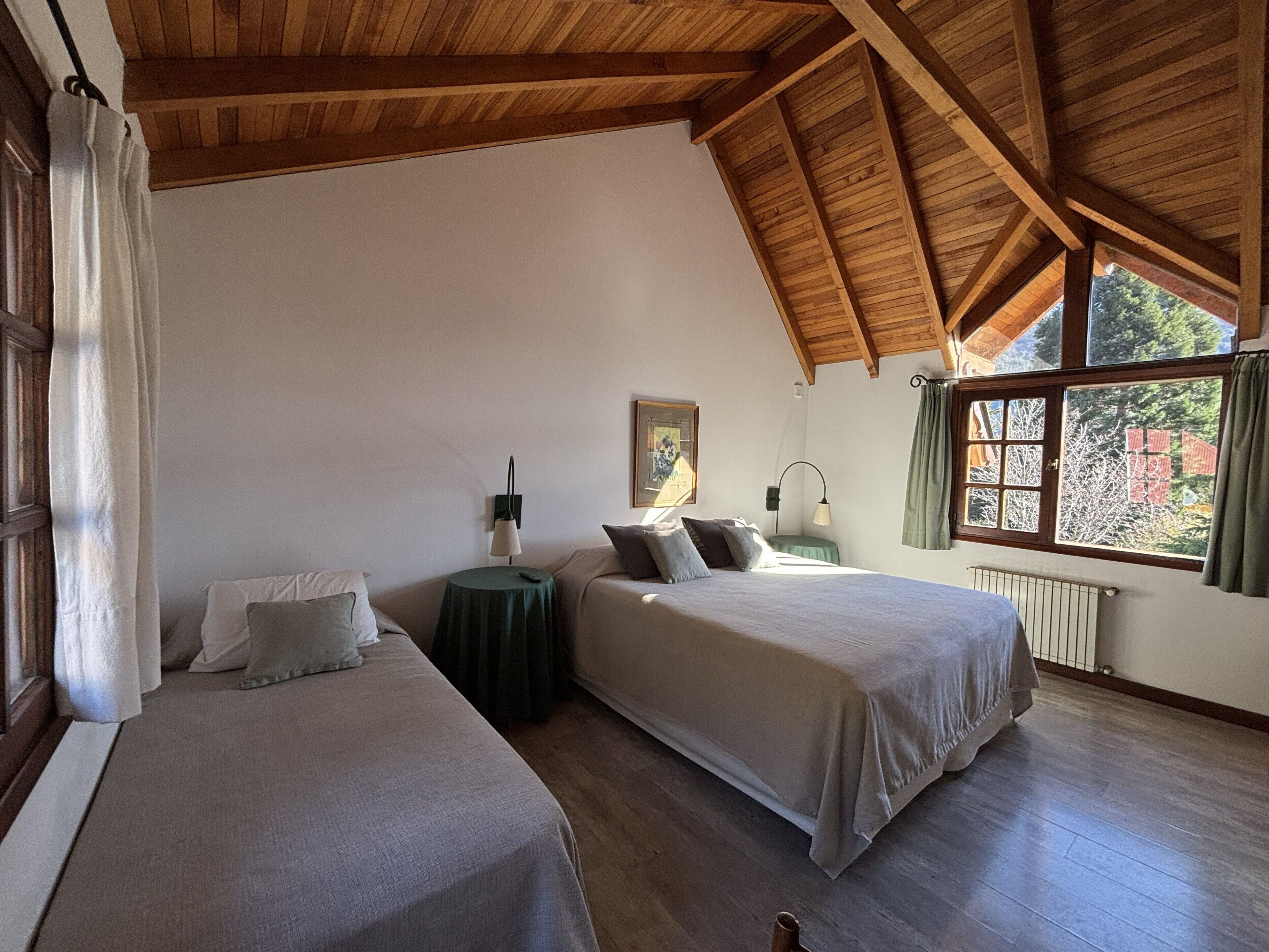 A bedroom with two beds, a small table, a lamp, and a window with curtains.