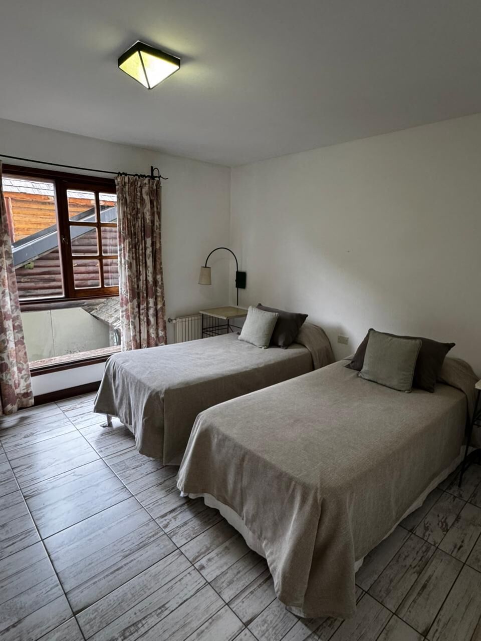 A room with two beds, a desk, a lamp, and a window with curtains.