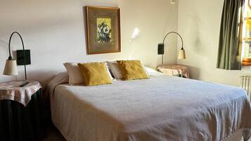 Un dormitorio con una cama grande, dos mesitas de noche, una mesilla auxiliar, un cuadro en la pared y una ventana con cortinas.