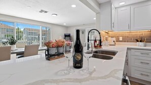 A modern kitchen with a large island, white cabinetry, and a view of the outdoors. - 4BR Waterfront | Boat Dock + Pool | 11-Min Walk to Beach | Sleeps 8 (Hudson)