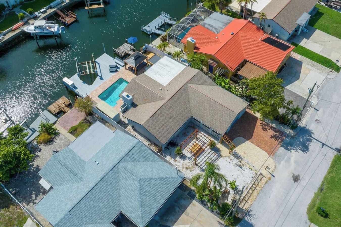 Un quartier résidentiel avec une piscine, des bateaux amarrés et une maison au toit rouge.