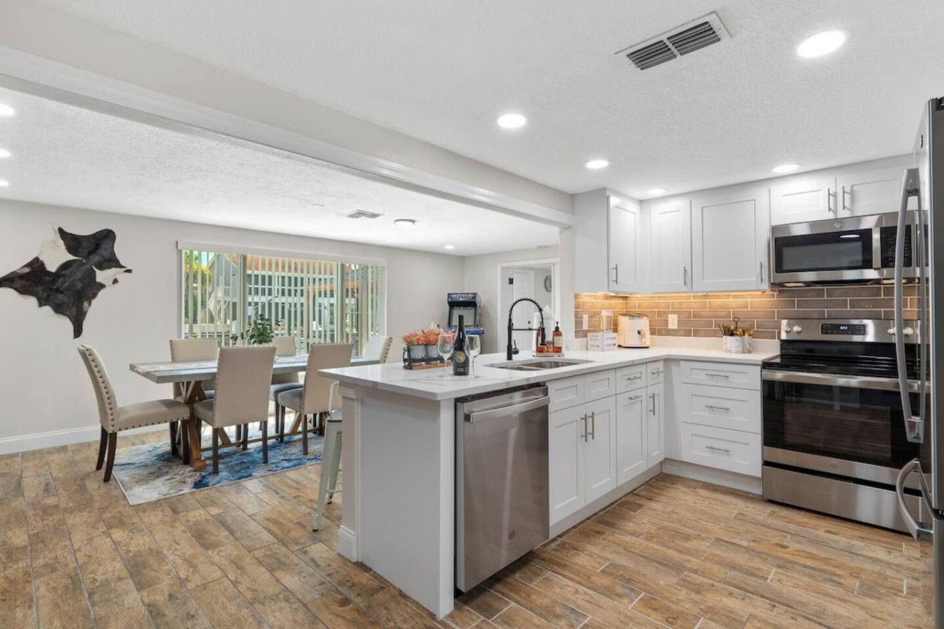 A modern kitchen with white cabinets, stainless steel appliances, and a dining area with a table and chairs.