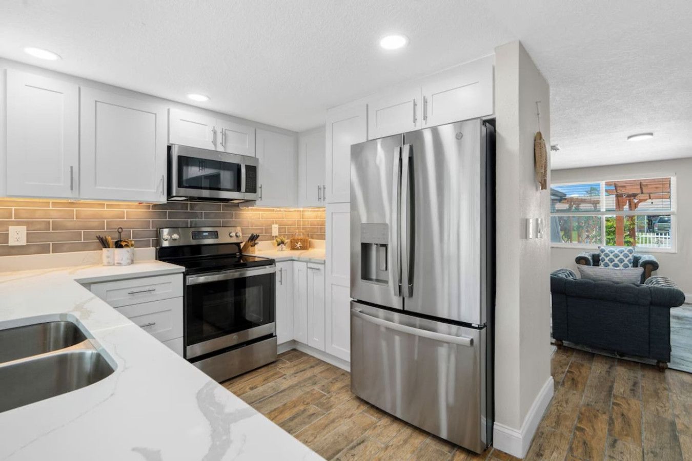 A modern kitchen with stainless steel appliances, white cabinetry, and a herringbone-patterned backsplash.