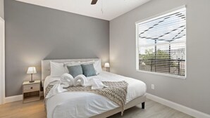 Un dormitorio con una cama, dos mesitas de noche con lámparas, un ventilador de techo y una ventana con persianas.
