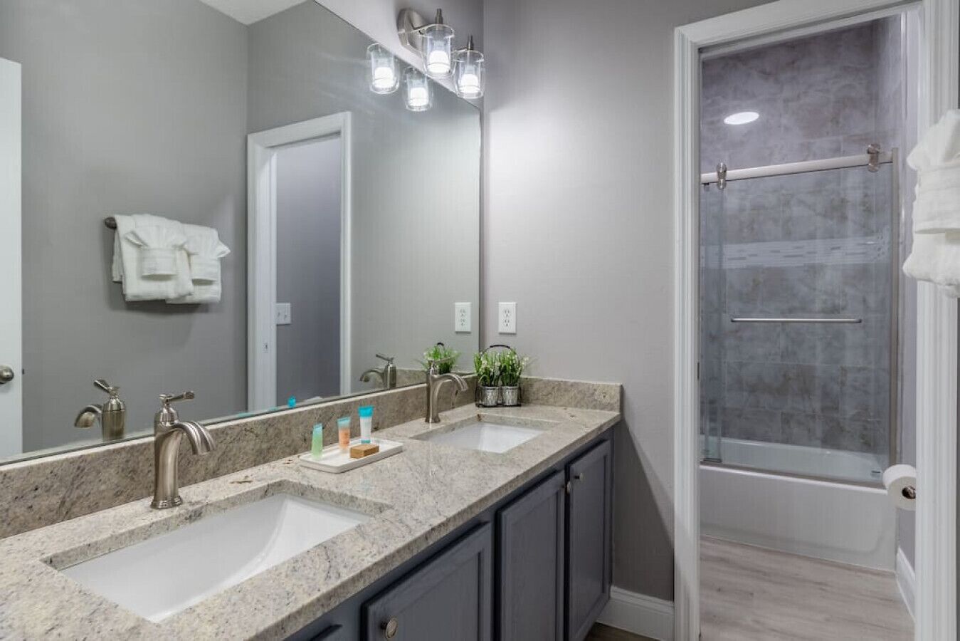 A bathroom with a double sink, a large mirror, a shower with a glass door, and a towel rack.