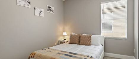 A bedroom with a bed, a nightstand, a lamp, and a window with blinds.