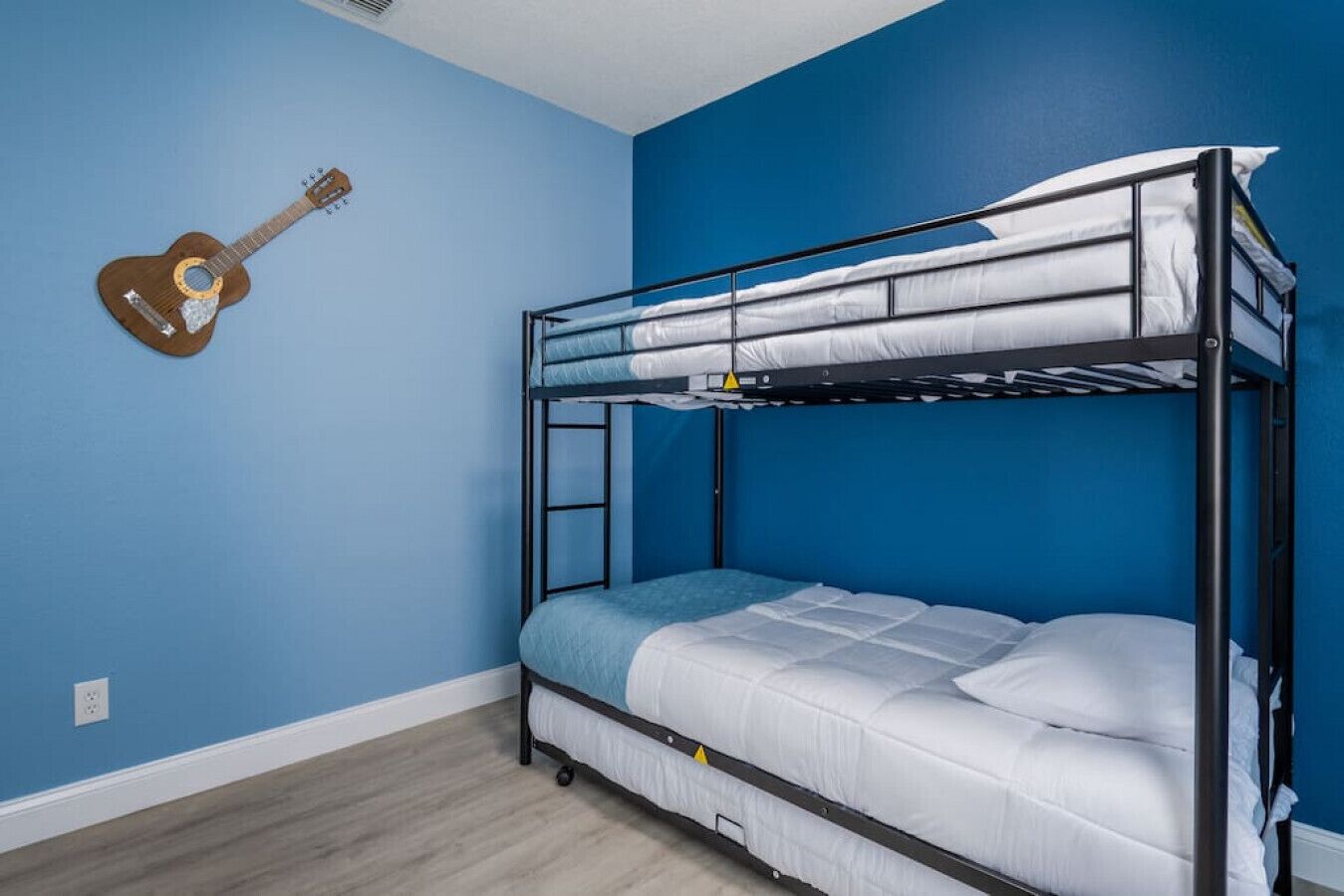 A bunk bed room with blue walls, a guitar on the wall, and a wooden floor.