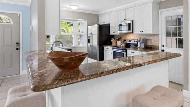 A modern kitchen with white cabinets, a granite countertop, a stainless steel refrigerator, and a large island with a copper bowl. - 3BR | Saltwater Pool + Spa | Solar Heated | 9 Min to Airport | Sleeps 7 (Clearwater)