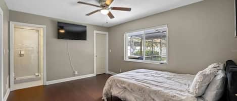 Ein Schlafzimmer mit Bett, Deckenventilator, Wand-Fernseher und Fenster mit Blick ins Freie.