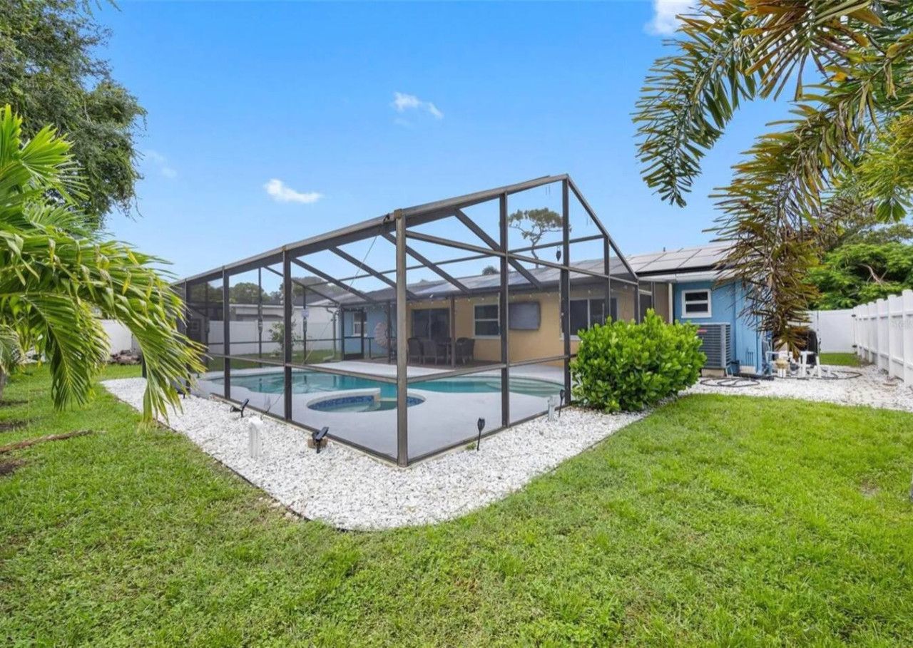 A house with a covered swimming pool, a lawn, and a blue house in the background.