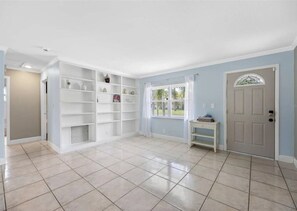 Una habitación amplia con suelo de baldosas, estanterías blancas y una puerta con ventana, además de una pequeña mesa.
