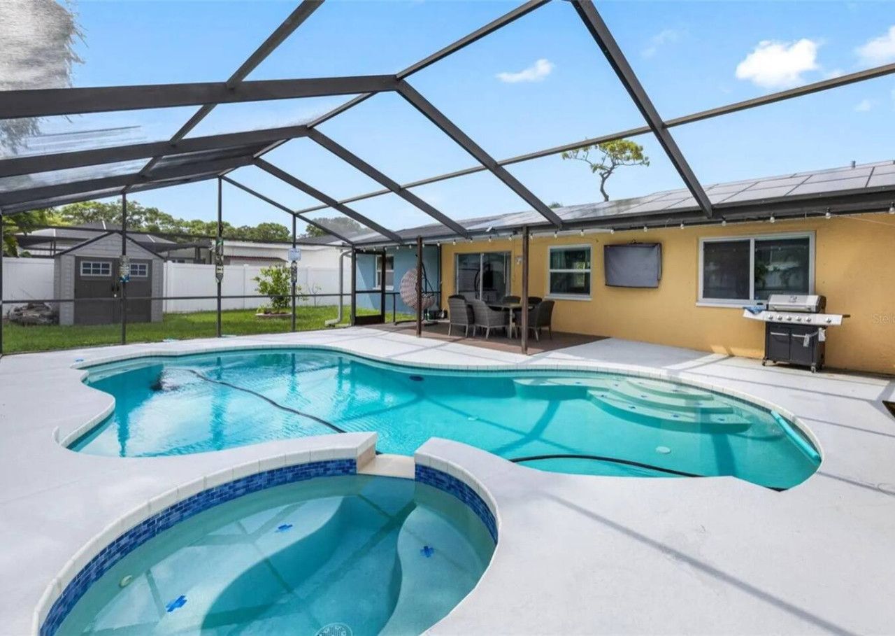 Une piscine dotée d’une structure servant de parasol, d’un espace barbecue et d’un patio couvert.