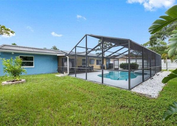 Un patio trasero con piscina, un porche cubierto y una casa.