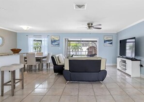 A spacious living area with a sofa, dining table, chairs, a TV, and a ceiling fan. - 3BR | Saltwater Pool + Spa | Solar Heated | 9 Min to Airport | Sleeps 7 (Clearwater)