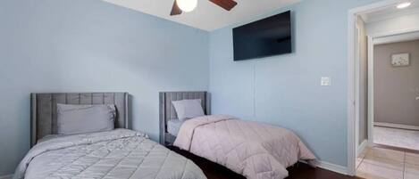Une chambre avec deux lits, un ventilateur de plafond et un téléviseur à écran plat fixé au mur.