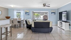 A spacious living area with a sofa, dining table, chairs, a TV, and a ceiling fan. - 3BR | Saltwater Pool + Spa | Solar Heated | 9 Min to Airport | Sleeps 7 (Clearwater)