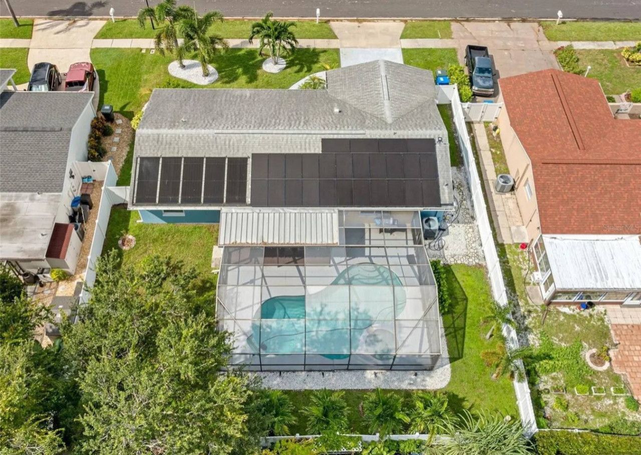 Una casa residencial con una gran piscina, paneles solares y un césped bien cuidado.