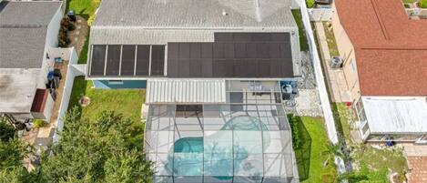 Una casa residencial con una gran piscina, paneles solares y un césped bien cuidado.