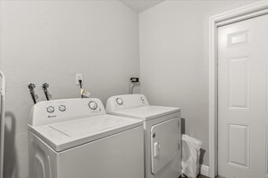 A laundry room with two white front-loading washers and dryers, a white door, and a white wall. - 4BR | Screened Pool | Next to Park | 10 Min Indian Rocks Beach | Sleeps 10 (Largo)