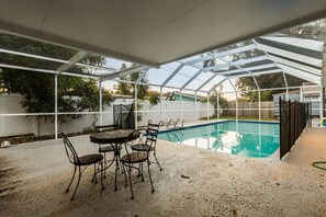 Un espacio al aire libre techado con piscina, una mesa con sillas y una valla.