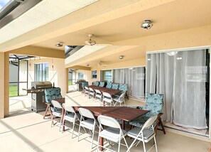 Eine Terrasse im Freien mit Grill, mehreren Tischen und Stühlen und Blick ins Grüne.