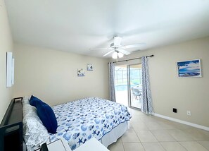 Ein Schlafzimmer mit Bett, Deckenventilator, einem Fenster mit Vorhängen und Blick ins Freie.