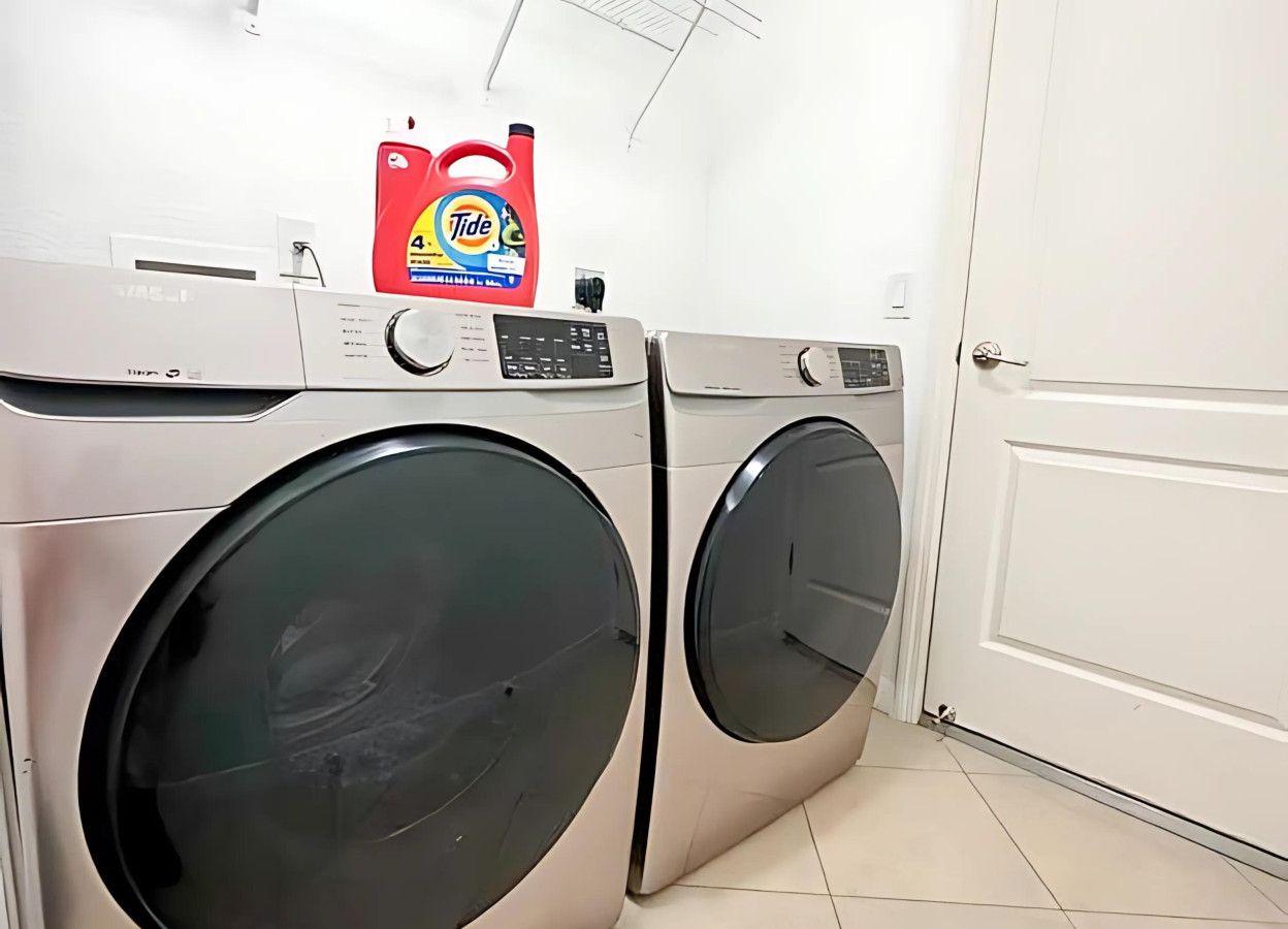 Une buanderie équipée de deux machines à laver à chargement frontal, avec une bouteille de lessive Tide rouge posée sur le dessus.