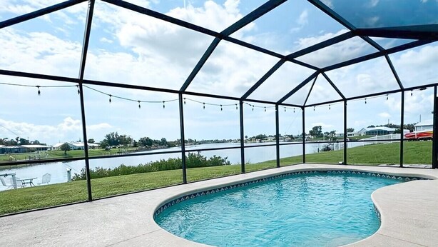 A covered swimming pool with a view of a lake and distant buildings. - 3BR Waterfront Views | Pool + BBQ | 3 King Beds | Sleeps 7 | Port Charlotte (Port Charlotte)