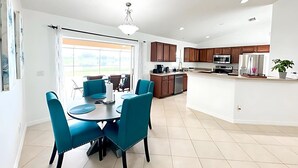 A modern kitchen with dark wooden cabinets, a central island, and a dining area with blue chairs and a round table. - 3BR Waterfront Views | Pool + BBQ | 3 King Beds | Sleeps 7 | Port Charlotte (Port Charlotte)